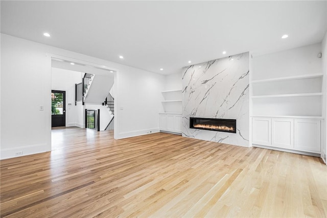 unfurnished living room with built in features, recessed lighting, stairway, a premium fireplace, and light wood-style floors