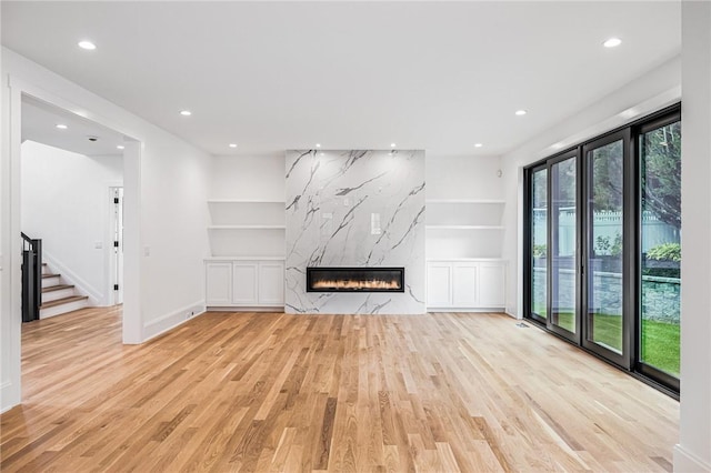 unfurnished living room featuring built in features, a premium fireplace, stairway, light wood-type flooring, and recessed lighting