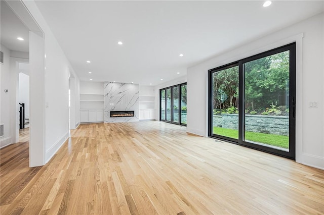 unfurnished living room featuring recessed lighting, a premium fireplace, visible vents, baseboards, and light wood-style floors