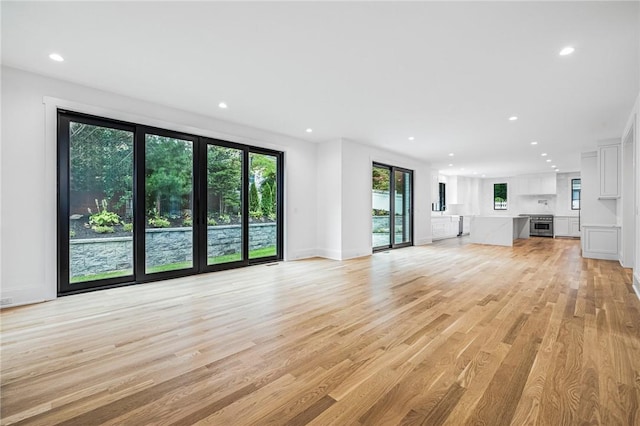 unfurnished living room with recessed lighting, baseboards, and light wood finished floors