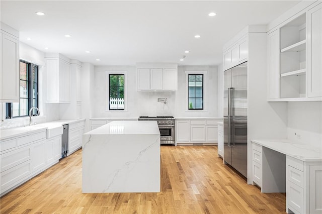 kitchen featuring light stone counters, a center island, high end appliances, light wood-style flooring, and white cabinets