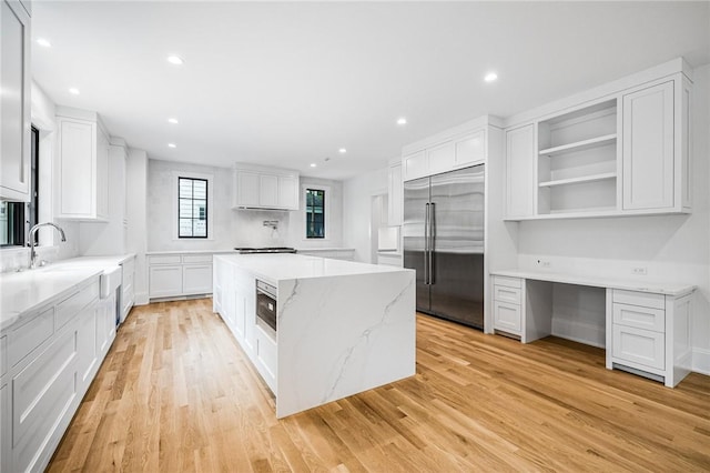 kitchen with a kitchen island, white cabinetry, open shelves, built in desk, and built in fridge