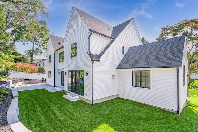 rear view of property with roof with shingles, a yard, and fence