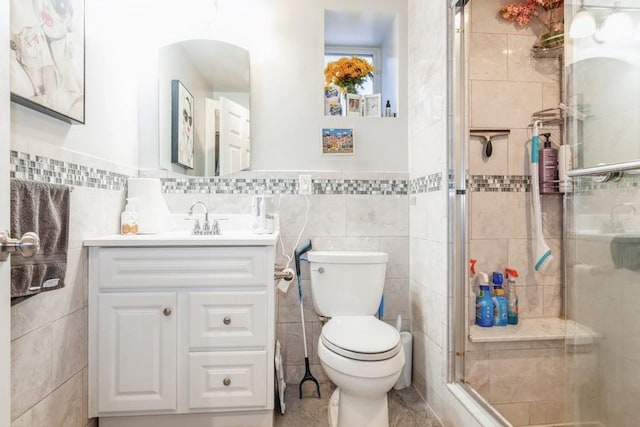 bathroom featuring vanity, toilet, a shower with door, and tile walls