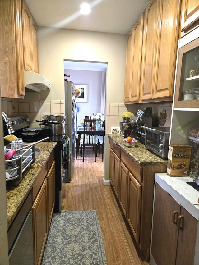 kitchen featuring wood-type flooring, appliances with stainless steel finishes, light stone counters, and decorative backsplash