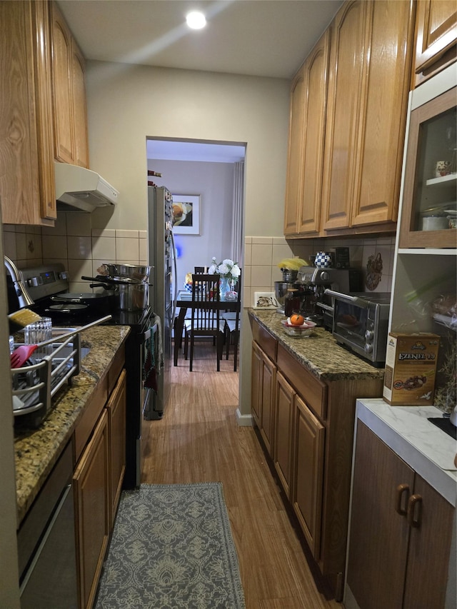 kitchen featuring dark wood-type flooring, appliances with stainless steel finishes, light stone counters, and backsplash