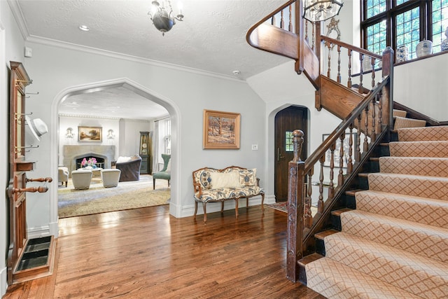 entryway featuring arched walkways, ornamental molding, a textured ceiling, and wood finished floors