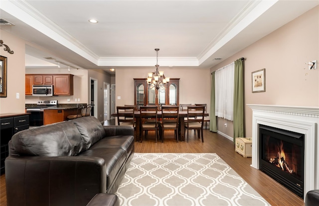 living room featuring a tray ceiling, light wood-type flooring, a chandelier, and crown molding