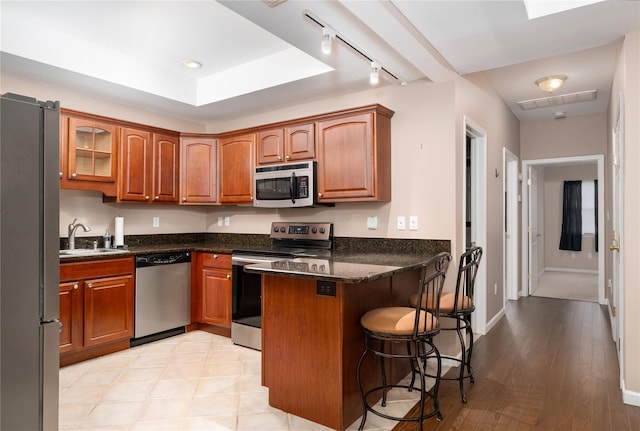 kitchen with a kitchen breakfast bar, stainless steel appliances, kitchen peninsula, sink, and dark stone countertops