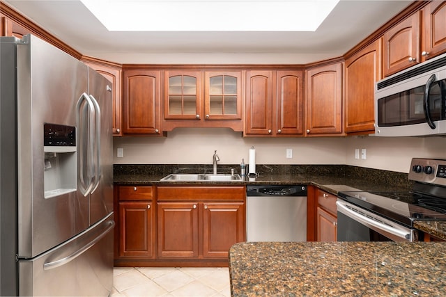 kitchen with appliances with stainless steel finishes, a skylight, dark stone counters, light tile patterned floors, and sink