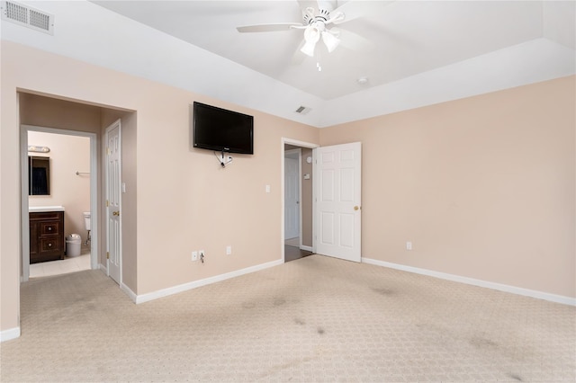 unfurnished bedroom with a tray ceiling, ensuite bathroom, light colored carpet, and lofted ceiling