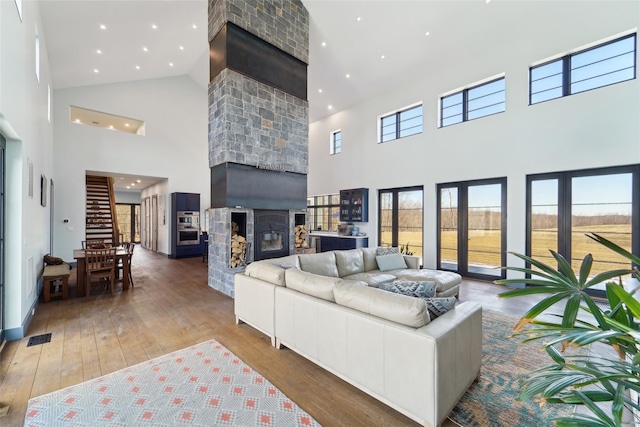living room with a fireplace, visible vents, a high ceiling, and hardwood / wood-style flooring