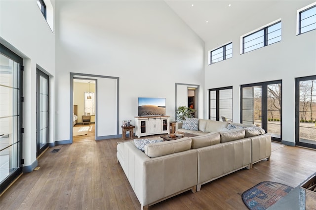living area with baseboards, visible vents, a high ceiling, and hardwood / wood-style floors
