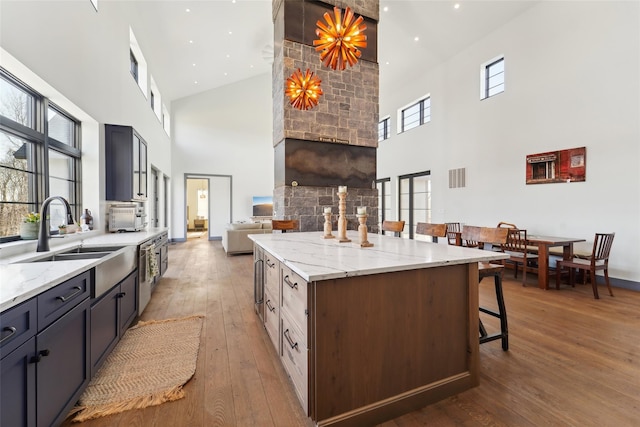 kitchen with light stone counters, hardwood / wood-style flooring, a sink, a breakfast bar, and a center island