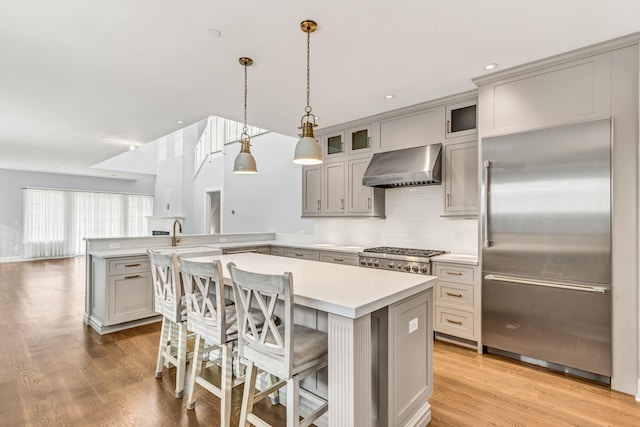 kitchen with a breakfast bar, built in refrigerator, a kitchen island, decorative light fixtures, and wall chimney exhaust hood