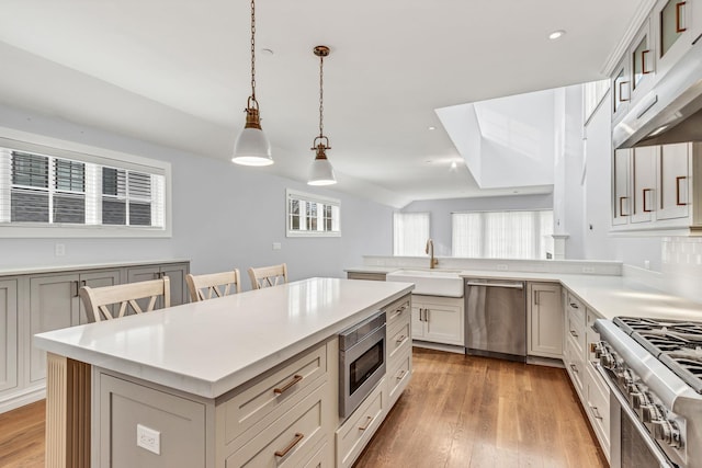 kitchen with a breakfast bar, pendant lighting, sink, stainless steel appliances, and light wood-type flooring