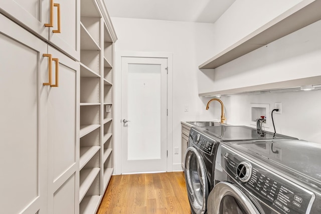 clothes washing area featuring cabinets, washer and dryer, sink, and light wood-type flooring