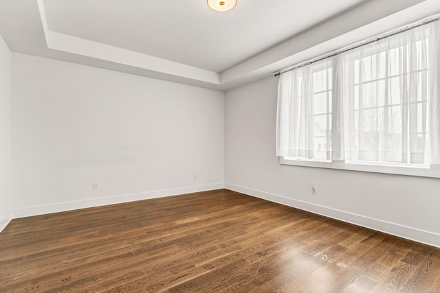 empty room with dark wood-type flooring and a raised ceiling