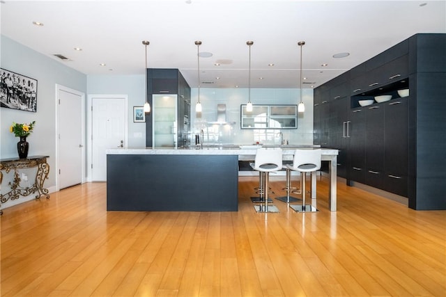 kitchen with a center island, a kitchen breakfast bar, pendant lighting, light hardwood / wood-style floors, and wall chimney range hood