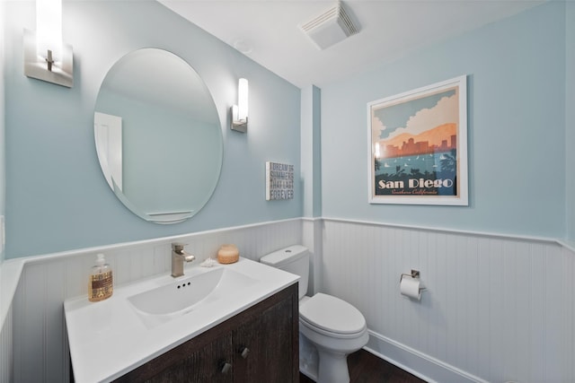 bathroom with a wainscoted wall, visible vents, toilet, vanity, and wood finished floors