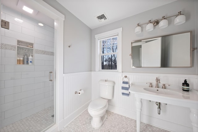 bathroom with a stall shower, visible vents, wainscoting, toilet, and tile patterned floors