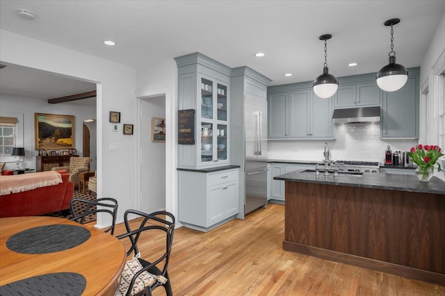 kitchen with glass insert cabinets, open floor plan, light wood-type flooring, under cabinet range hood, and pendant lighting