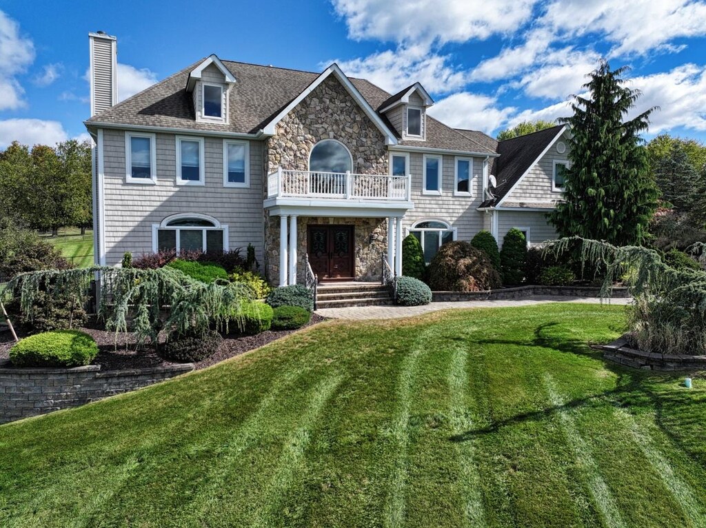 view of front of house featuring a balcony, a chimney, a front lawn, french doors, and stone siding
