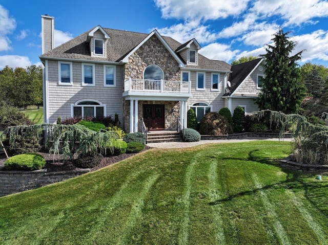 view of front of house featuring a balcony, a chimney, a front lawn, french doors, and stone siding