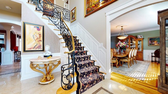 stairs with decorative columns, arched walkways, ornamental molding, wainscoting, and marble finish floor