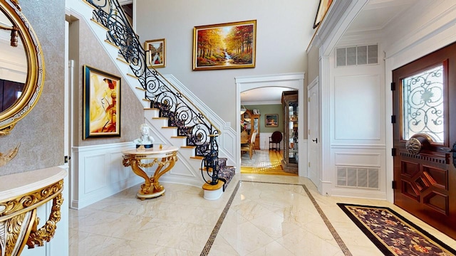 foyer featuring visible vents, arched walkways, crown molding, a decorative wall, and marble finish floor