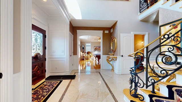 entryway featuring stairway, arched walkways, wainscoting, and a decorative wall