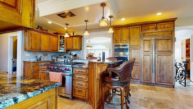 kitchen with stone tile flooring, high end appliances, arched walkways, and brown cabinets