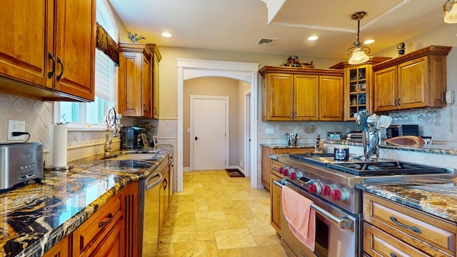 kitchen featuring brown cabinetry, visible vents, arched walkways, a sink, and stainless steel appliances