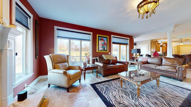 living area featuring a wealth of natural light, baseboards, ornate columns, and stone tile flooring