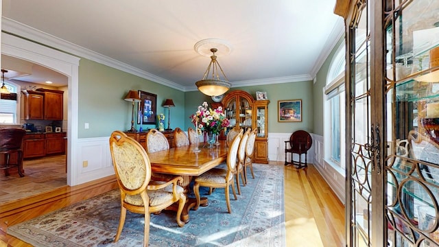 dining space with arched walkways, a wainscoted wall, light wood-style floors, and ornamental molding