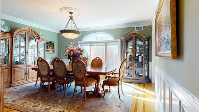 dining room featuring visible vents, wainscoting, wood finished floors, and ornamental molding