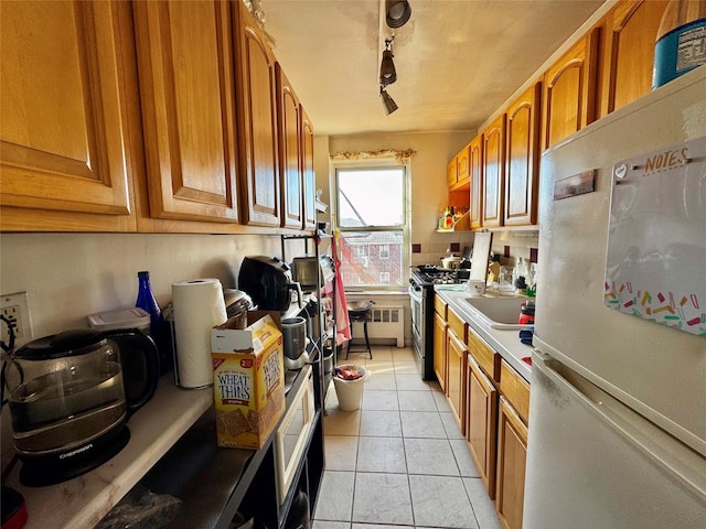 kitchen with stainless steel gas range oven, light tile patterned floors, track lighting, radiator, and white fridge