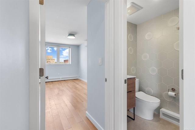 bathroom featuring hardwood / wood-style flooring, tile walls, a baseboard heating unit, vanity, and toilet