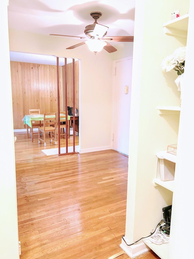 empty room with ceiling fan, light wood-type flooring, and wood walls