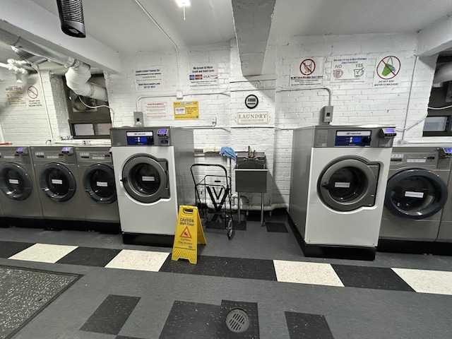 washroom with washing machine and dryer and brick wall