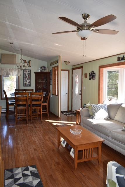 living area with lofted ceiling, hardwood / wood-style floors, and ceiling fan with notable chandelier