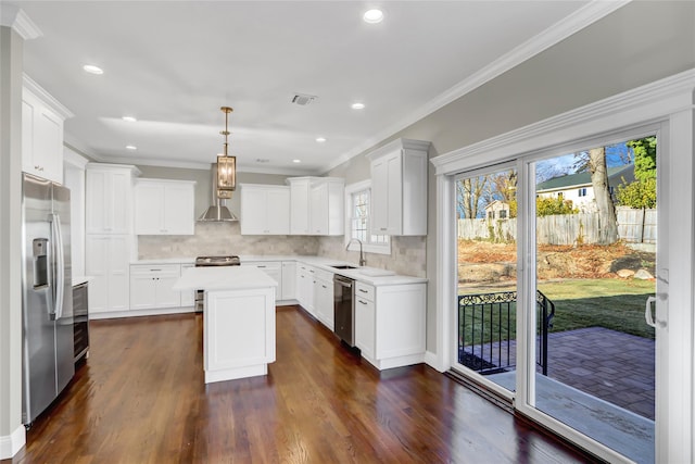 kitchen featuring appliances with stainless steel finishes, white cabinetry, a kitchen island, decorative light fixtures, and wall chimney exhaust hood