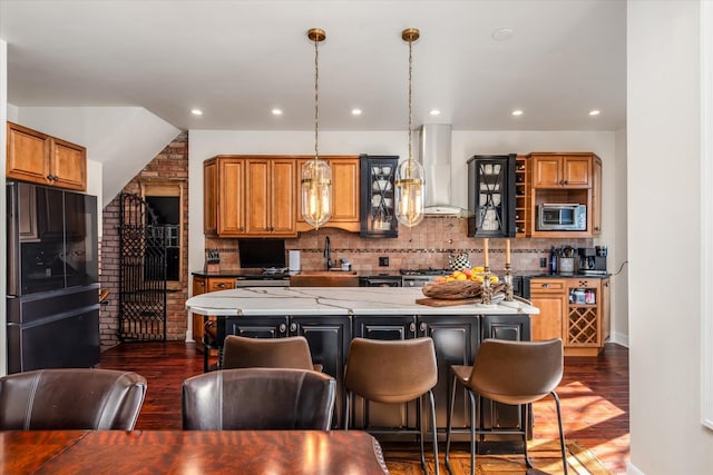 kitchen with stainless steel microwave, hanging light fixtures, a center island, black fridge, and wall chimney range hood