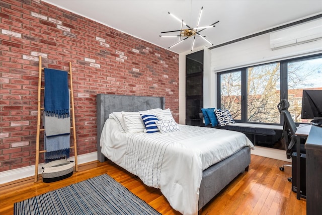 bedroom with brick wall, wood-type flooring, an AC wall unit, and ceiling fan with notable chandelier