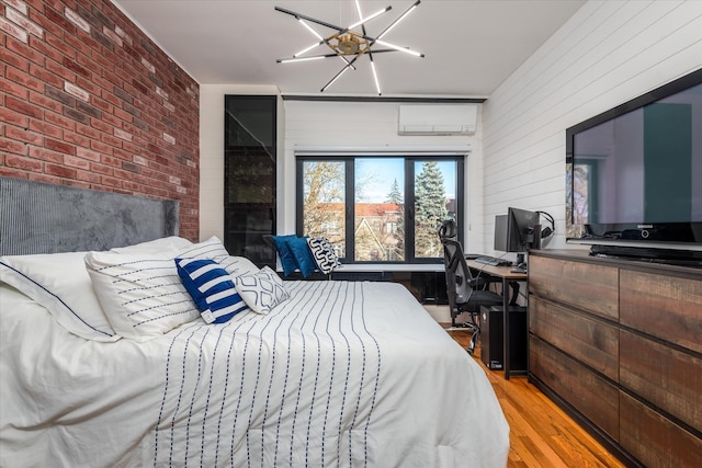 bedroom with brick wall, a wall mounted air conditioner, light hardwood / wood-style floors, and a notable chandelier