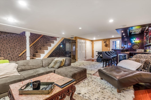 living room featuring bar, wine cooler, wood-type flooring, and brick wall