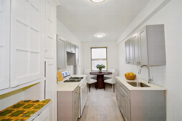 kitchen featuring light countertops, gray cabinets, white gas range, and a sink