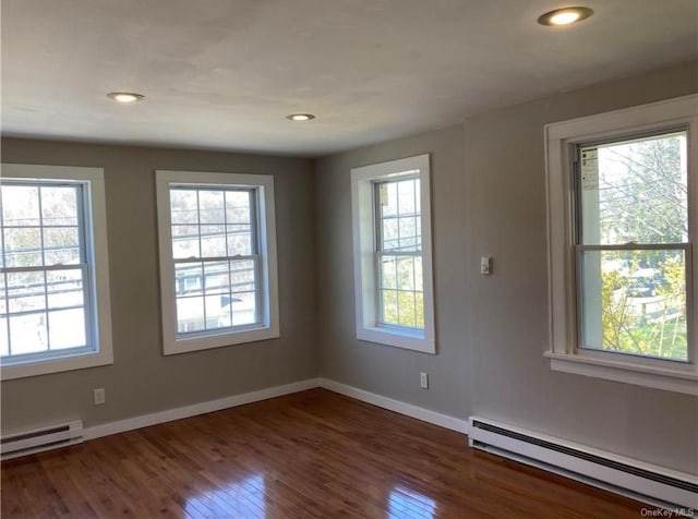 unfurnished room with a baseboard radiator, plenty of natural light, and dark wood-type flooring