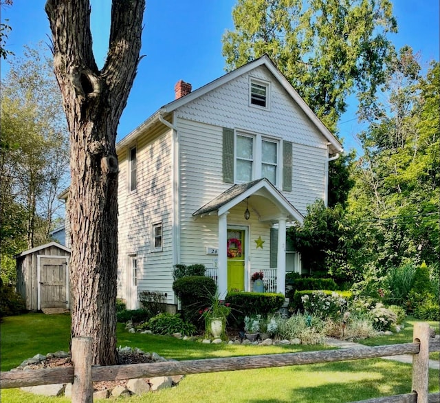 view of front facade featuring a chimney, a storage shed, an outdoor structure, and a front yard