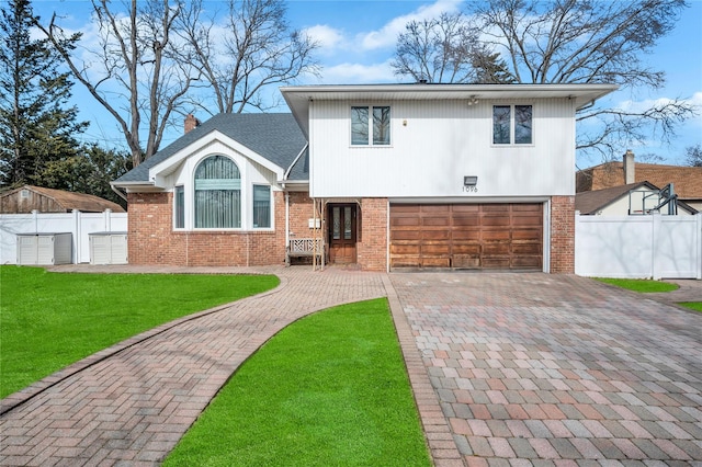 tri-level home featuring brick siding, a chimney, fence, decorative driveway, and a front yard